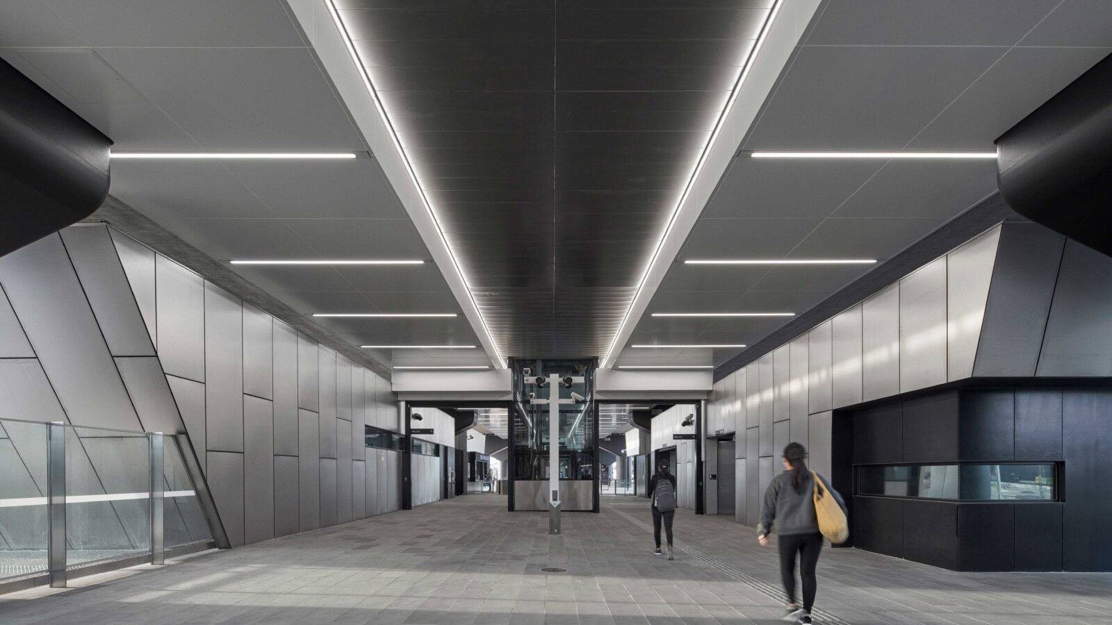 Ground-level public plaza beneath Reservoir Station’s elevated rail line, featuring angular architecture and integrated lighting by Genton in Melbourne