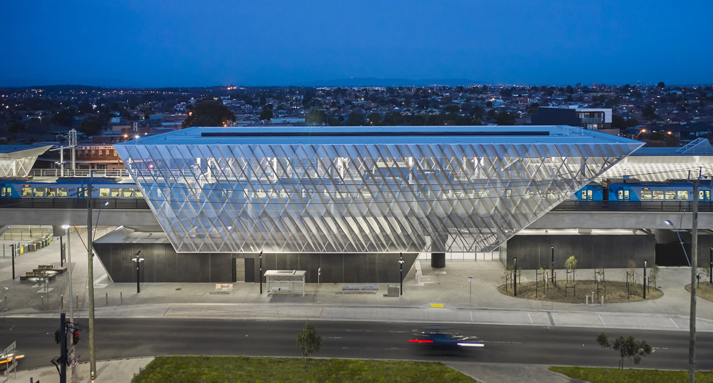Reservoir Station at dusk with illuminated translucent canopy and elevated rail platform – Genton-designed public transport hub in Melbourne