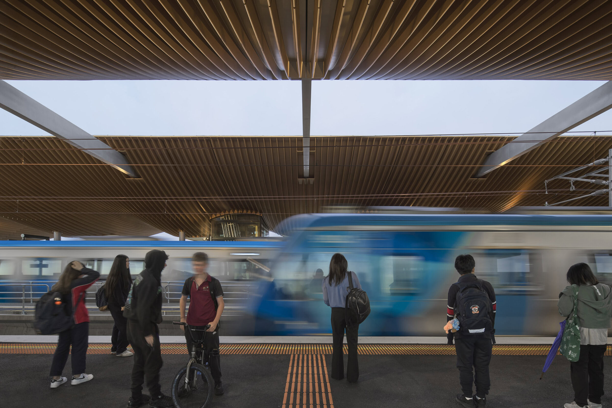 Pakenham Station Melbourne rail architecture with elevated platform, bronze soffit, and commuters waiting as train passes