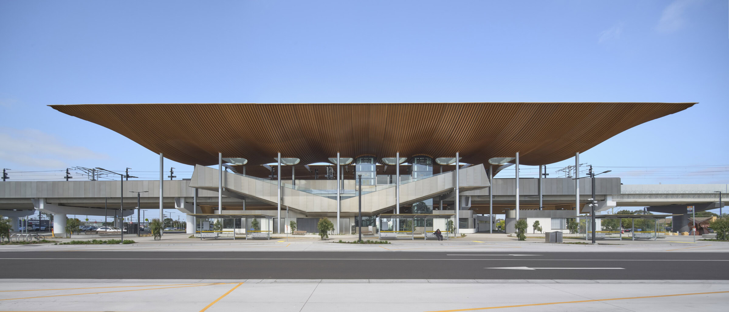 Pakenham Station Melbourne rail architecture with full-span bronze roof and elevated transparent structure under clear blue sky