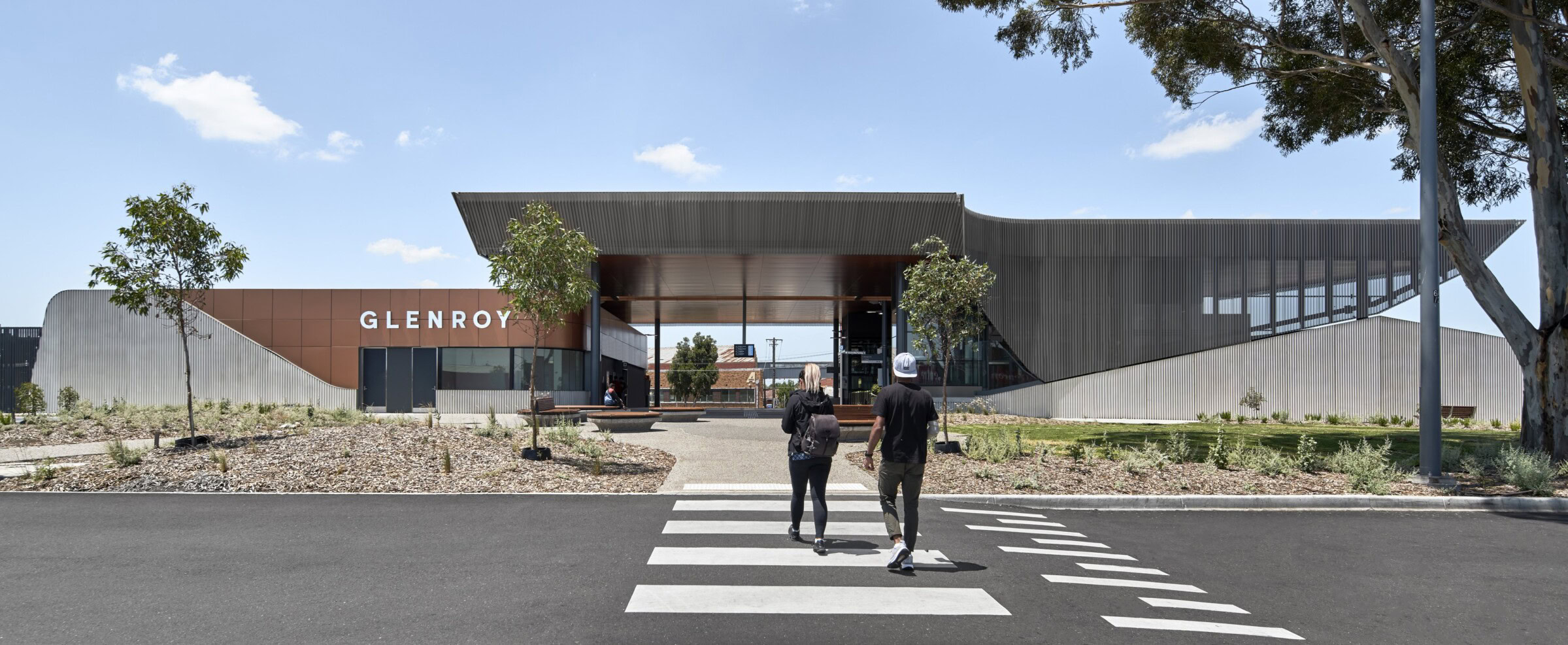 Pedestrians approaching Glenroy Station across a zebra crossing, showcasing Genton’s civic-oriented rail architecture