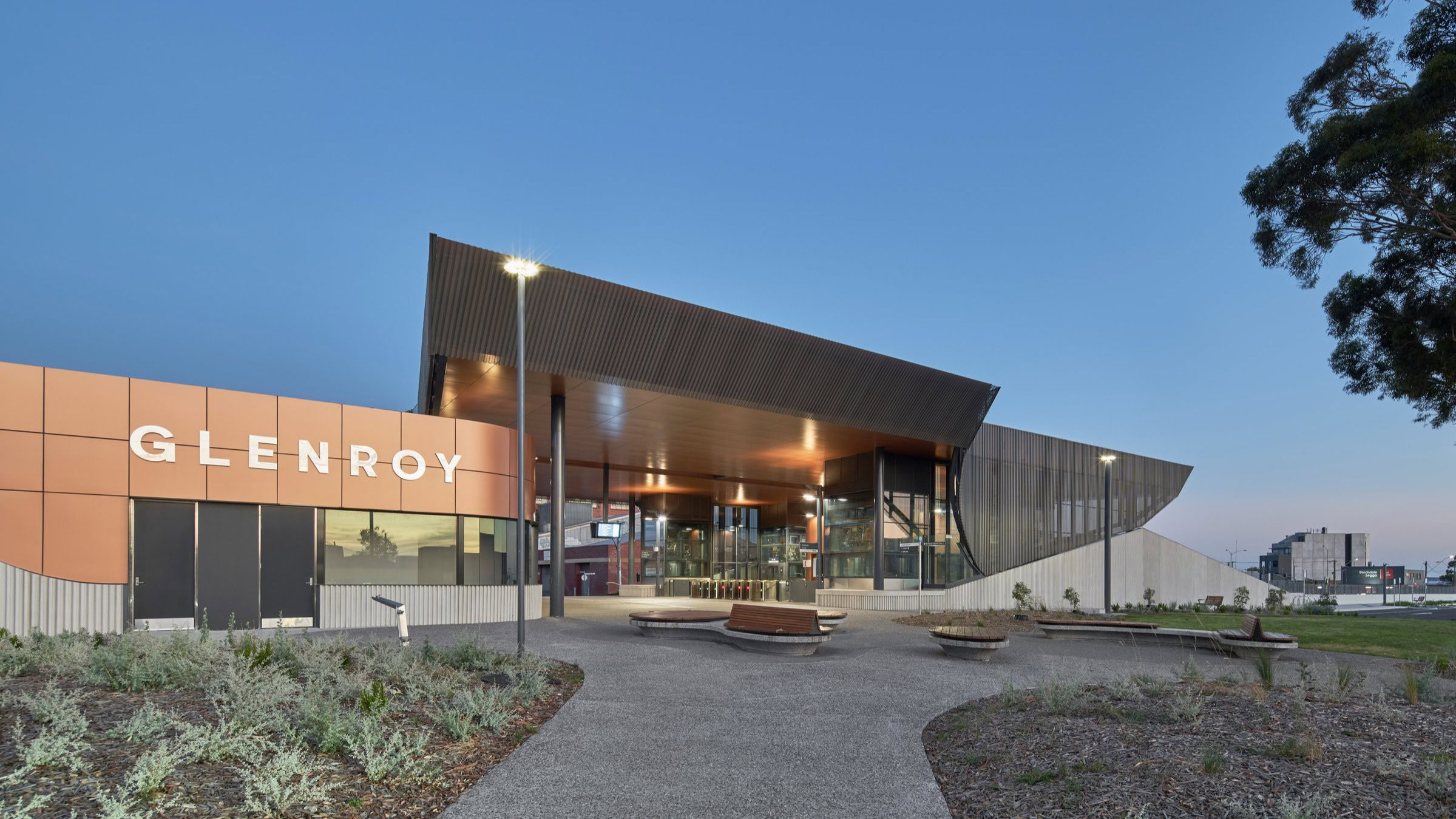 Entry to Glenroy Station Melbourne rail architecture at dusk with curved roof and public forecourt, part of Genton’s Melbourne rail infrastructure design