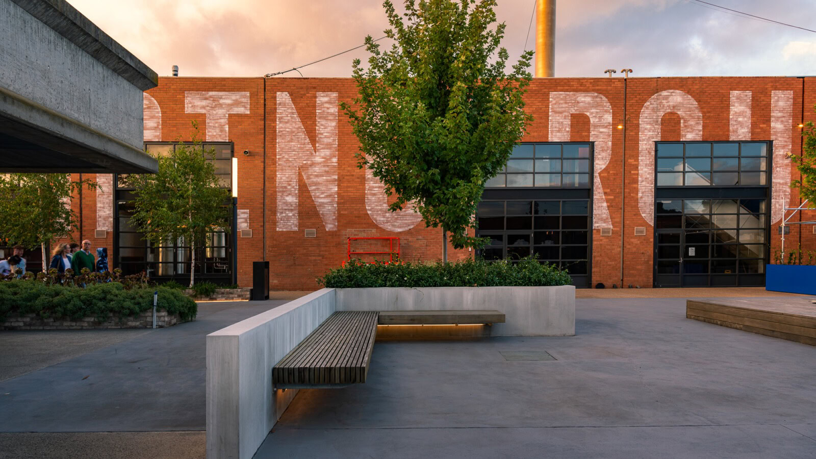 Public courtyard with seating and greenery in a mixed-use hospitality precinct at Morris Moor, featuring industrial brick facades and adaptive re-use architecture.