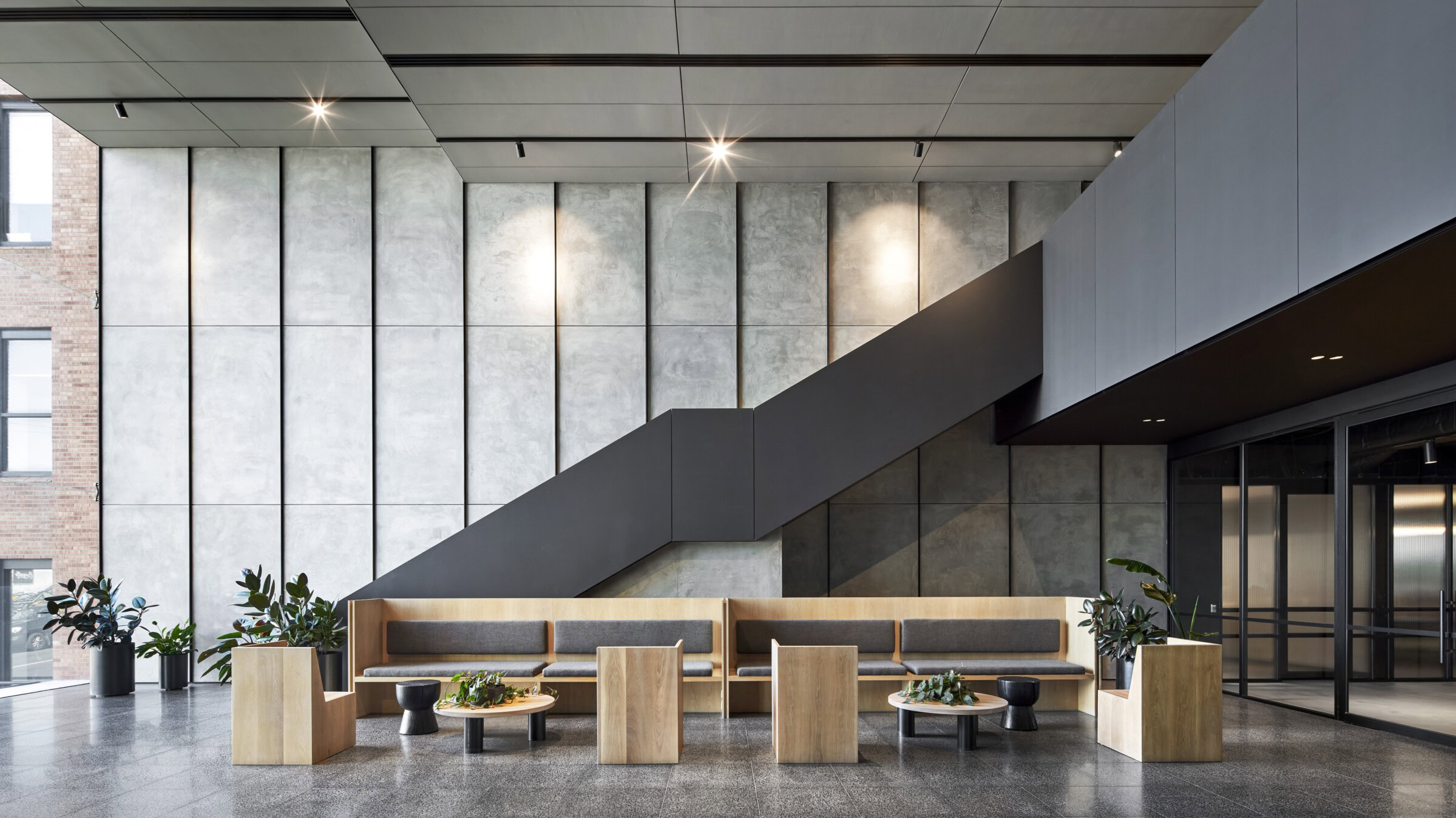 Contemporary interior of Morris Moor featuring polished concrete panels, a black steel staircase, timber and grey lounge seating, and greenery in a refined mixed-use hospitality setting.