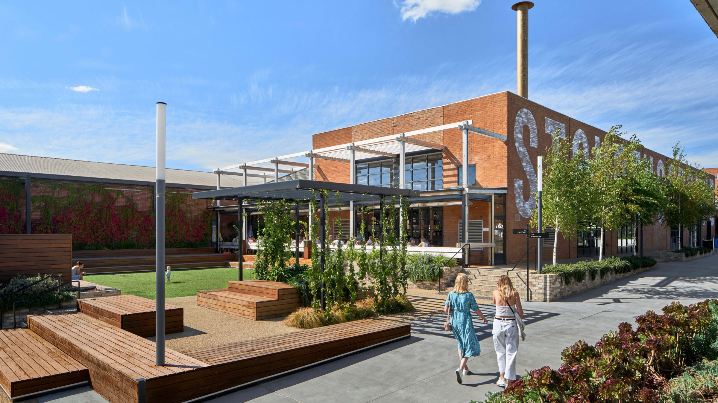 People walk through a landscaped public space at Morris Moor, a revitalised industrial site reimagined as a mixed-use hospitality and lifestyle precinct.